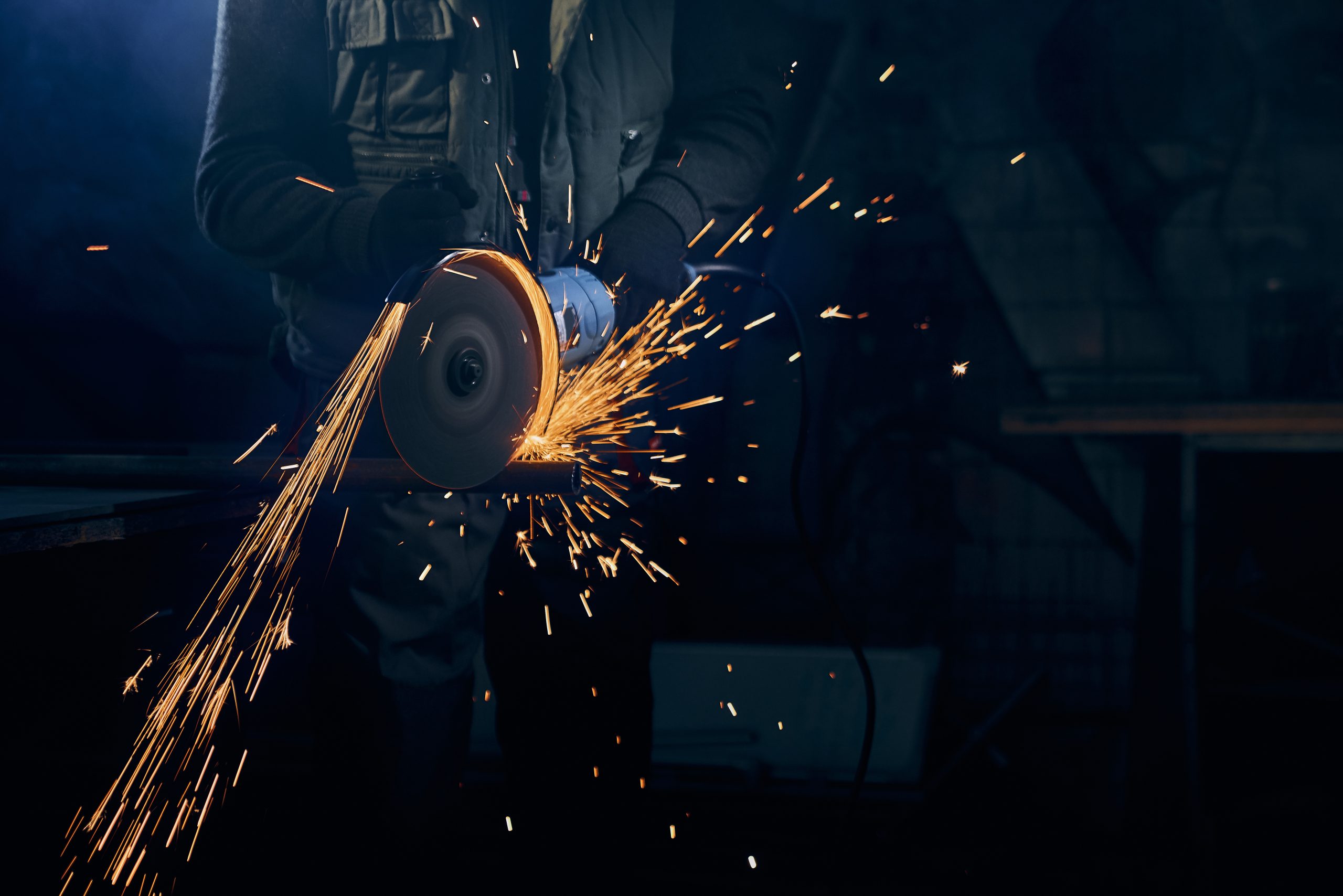 Close up of fitter in special suit cutting with rotating disc for metal with large sparks. Concept of process polishing or welding metal with flash sparks in factory.